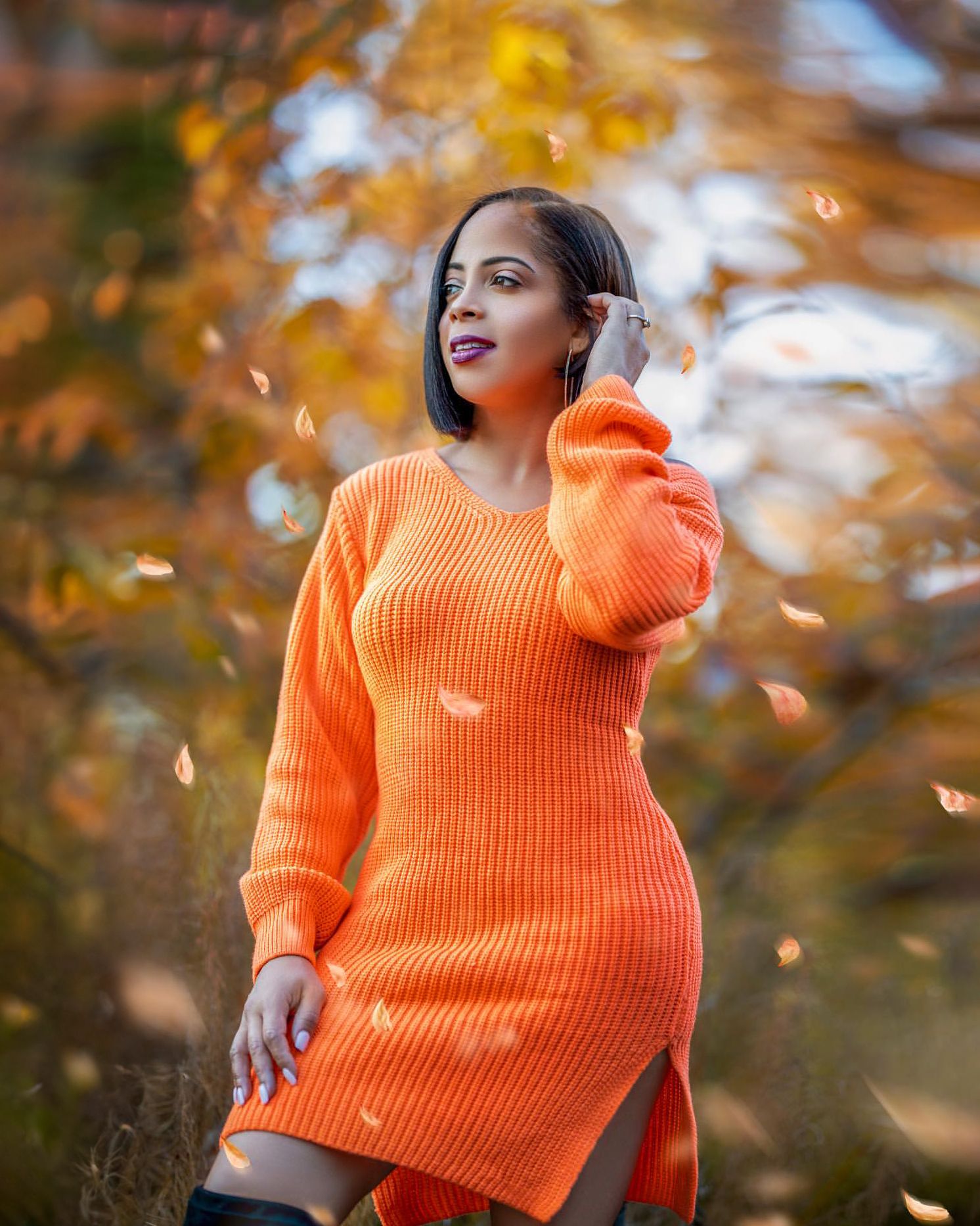 Autumn fashion portrait in orange sweater dress against fall foliage background.