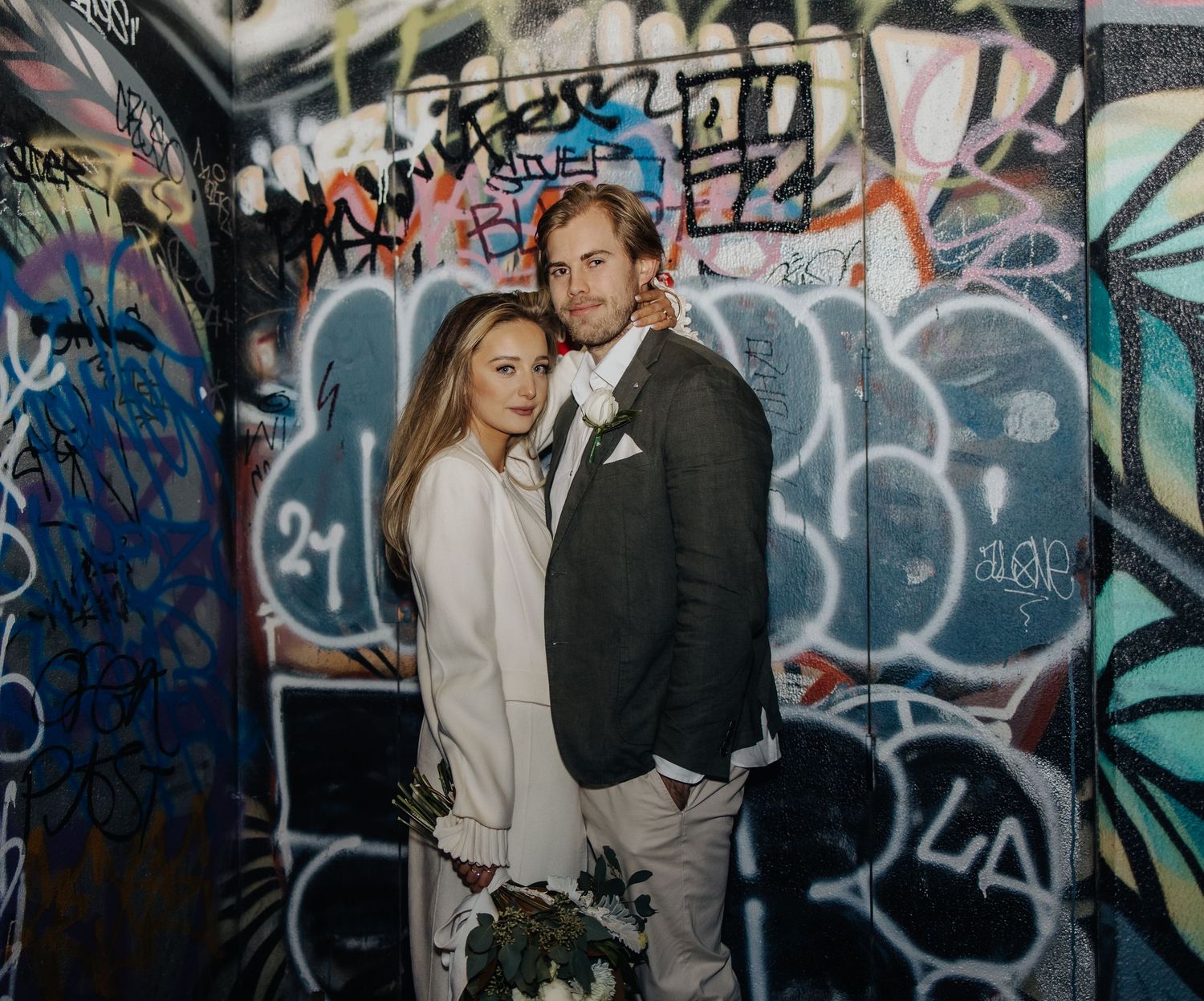 Romantic portrait session against a wall covered in vibrant street art and graffiti.