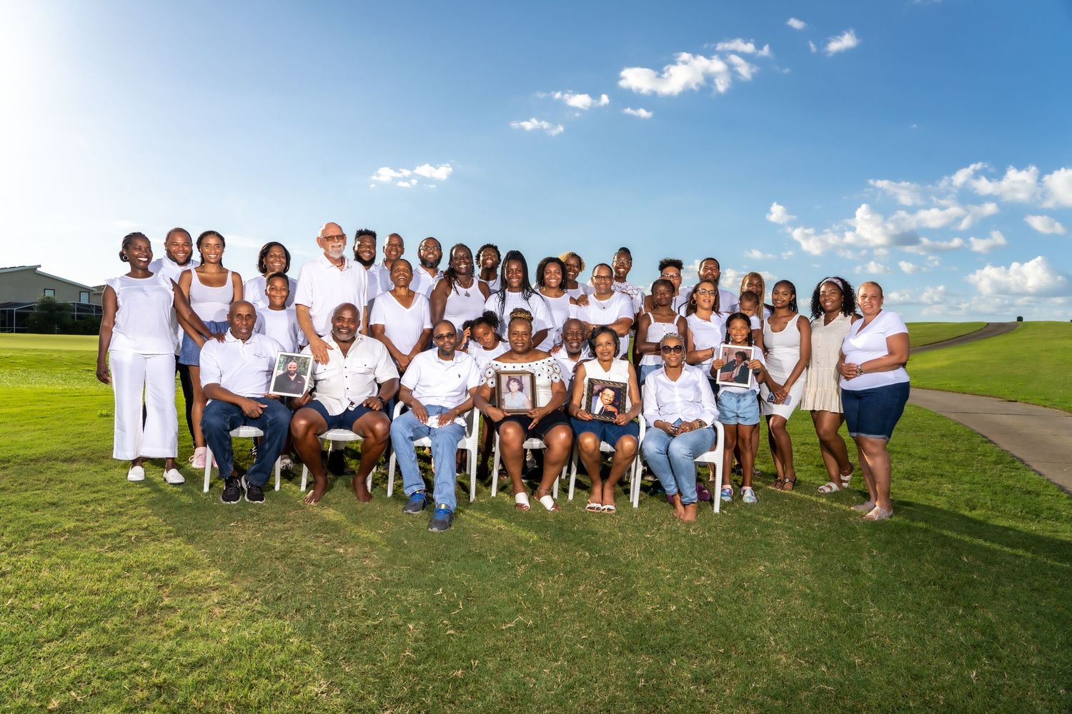 Large group in coordinated white outfits poses together on grassy field under blue sky.