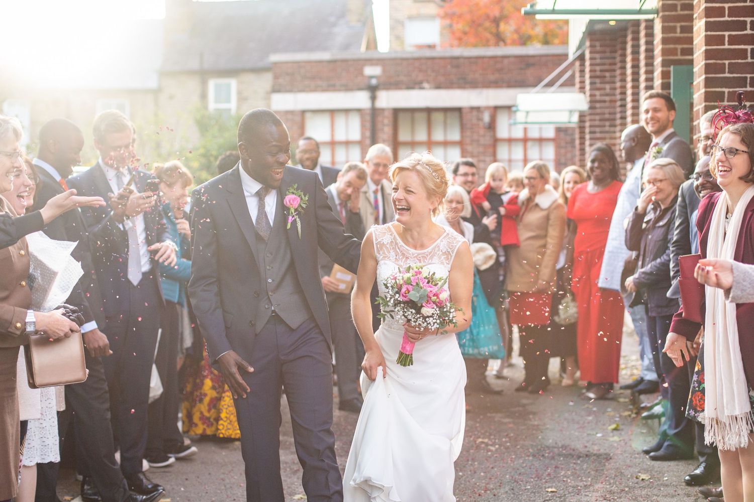 Happy newlyweds walk among cheering guests outside on their wedding day in golden sunlight.