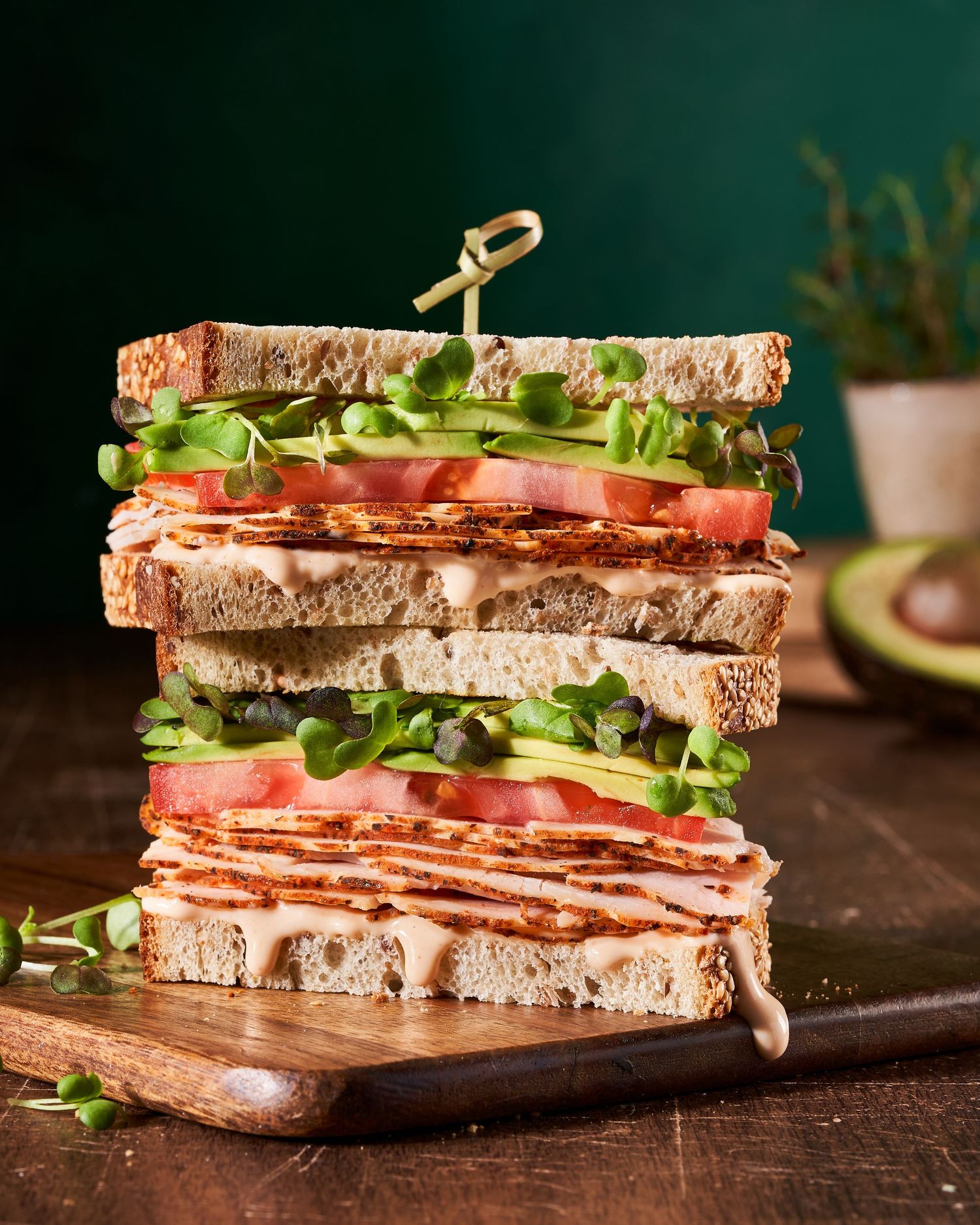 Fresh club sandwich with layers of meat, lettuce, and tomato on whole grain bread arranged on wooden cutting board.