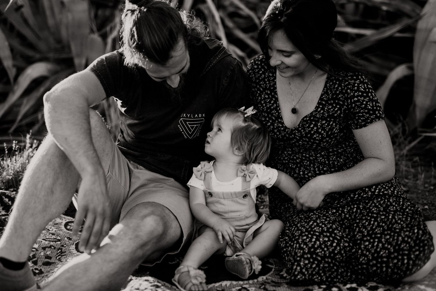 Intimate family moment captured on a blanket surrounded by tropical plants at sunset.