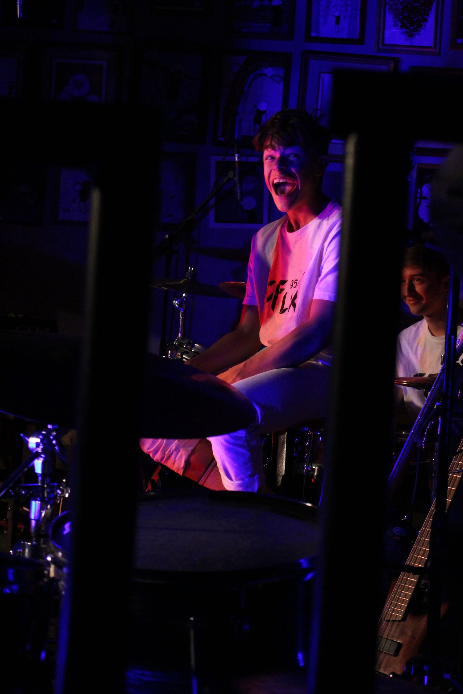 Young musician laughing joyfully while performing on stage under purple and pink lights in a dark venue.