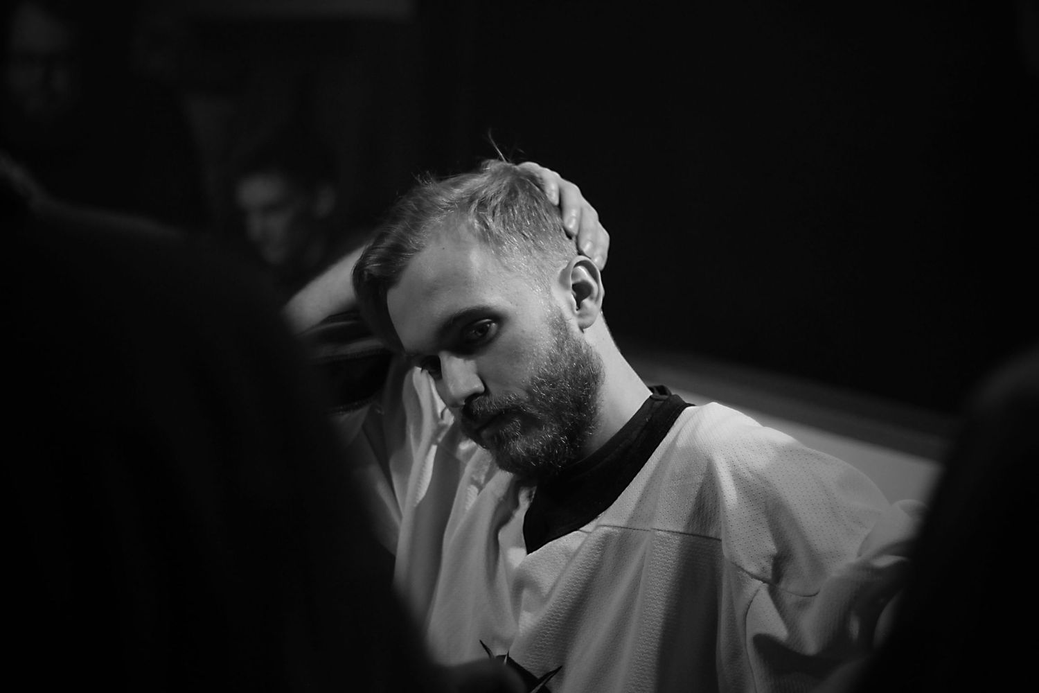 Black and white close-up of a bearded man running hand through hair in a dark setting.