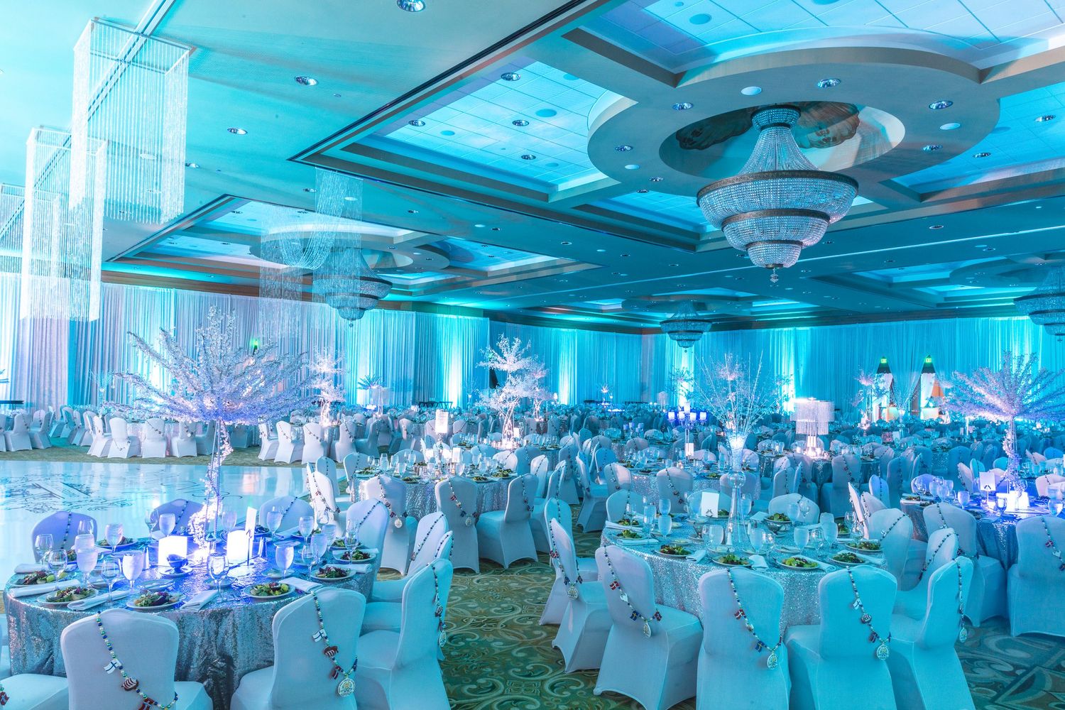 Elegant ballroom decorated in blue uplighting with white-draped tables and chairs.