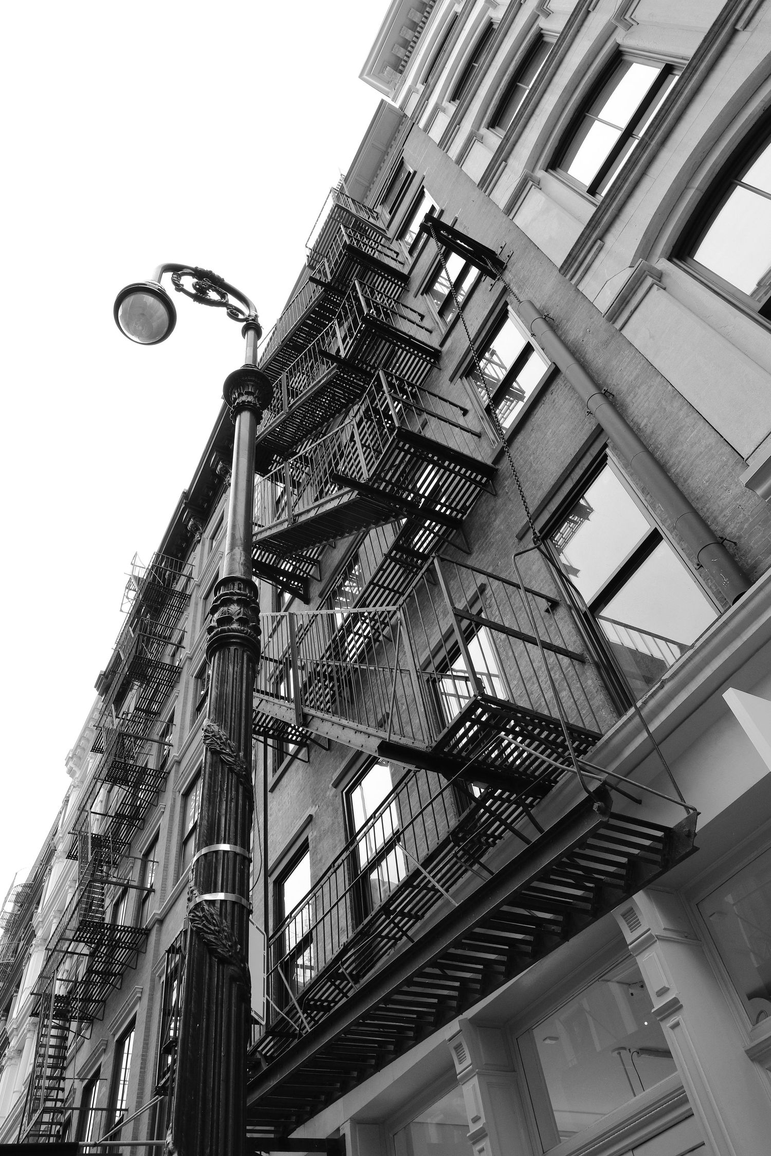 Classic New York City building facade with wrought iron fire escapes and street lamp in black and white.