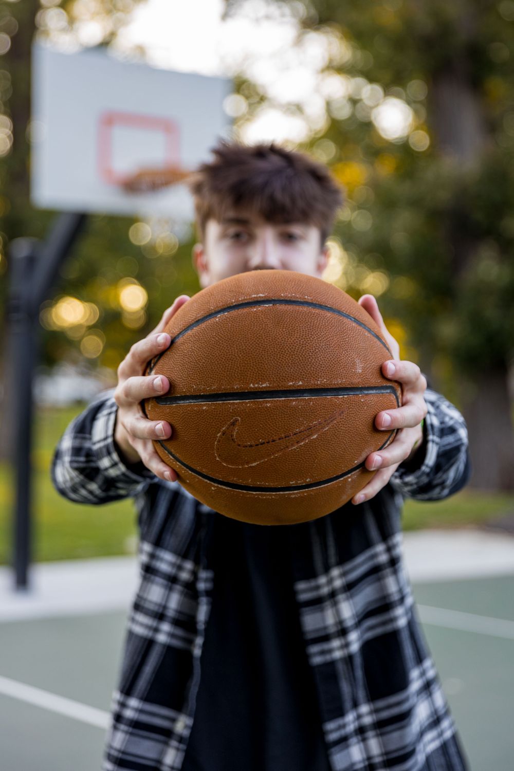 Person holding basketball in front of face on outdoor court at sunset.