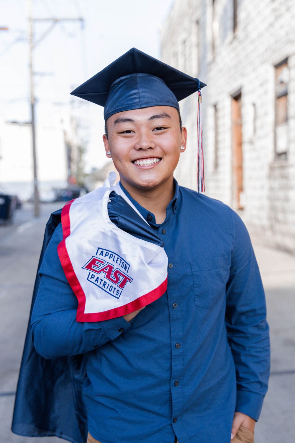 Graduate in blue cap and gown poses for portraits outside brick building.