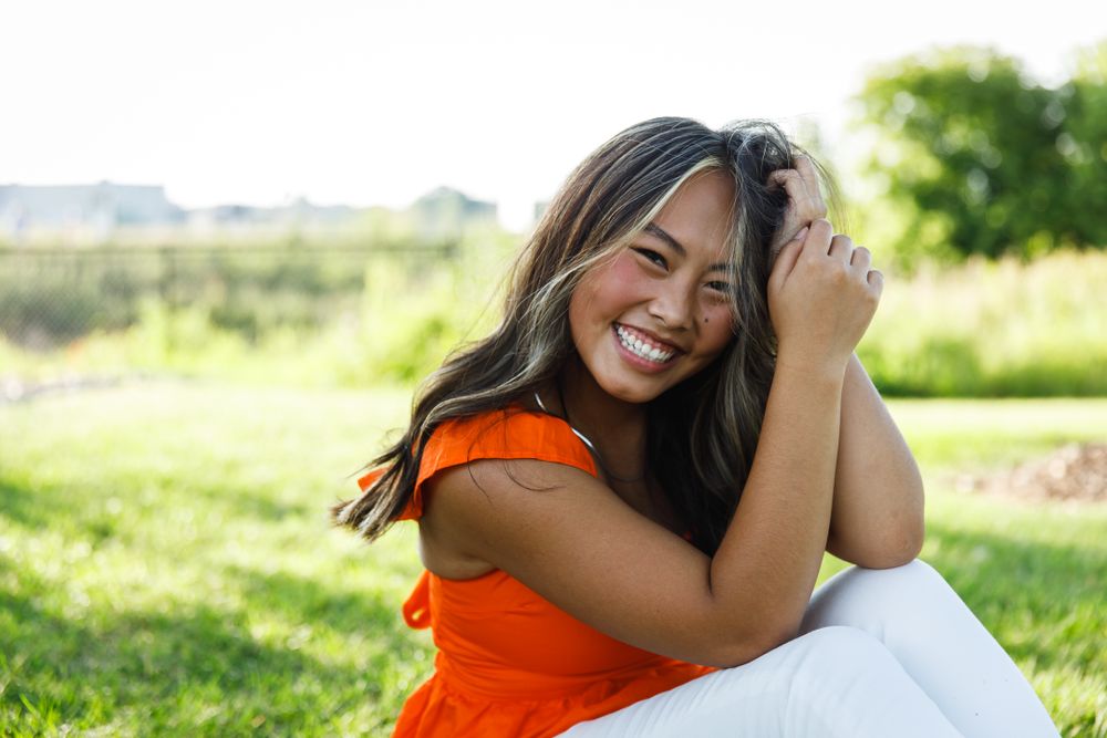 A person in an orange dress sits outdoors in a grassy field during golden hour.