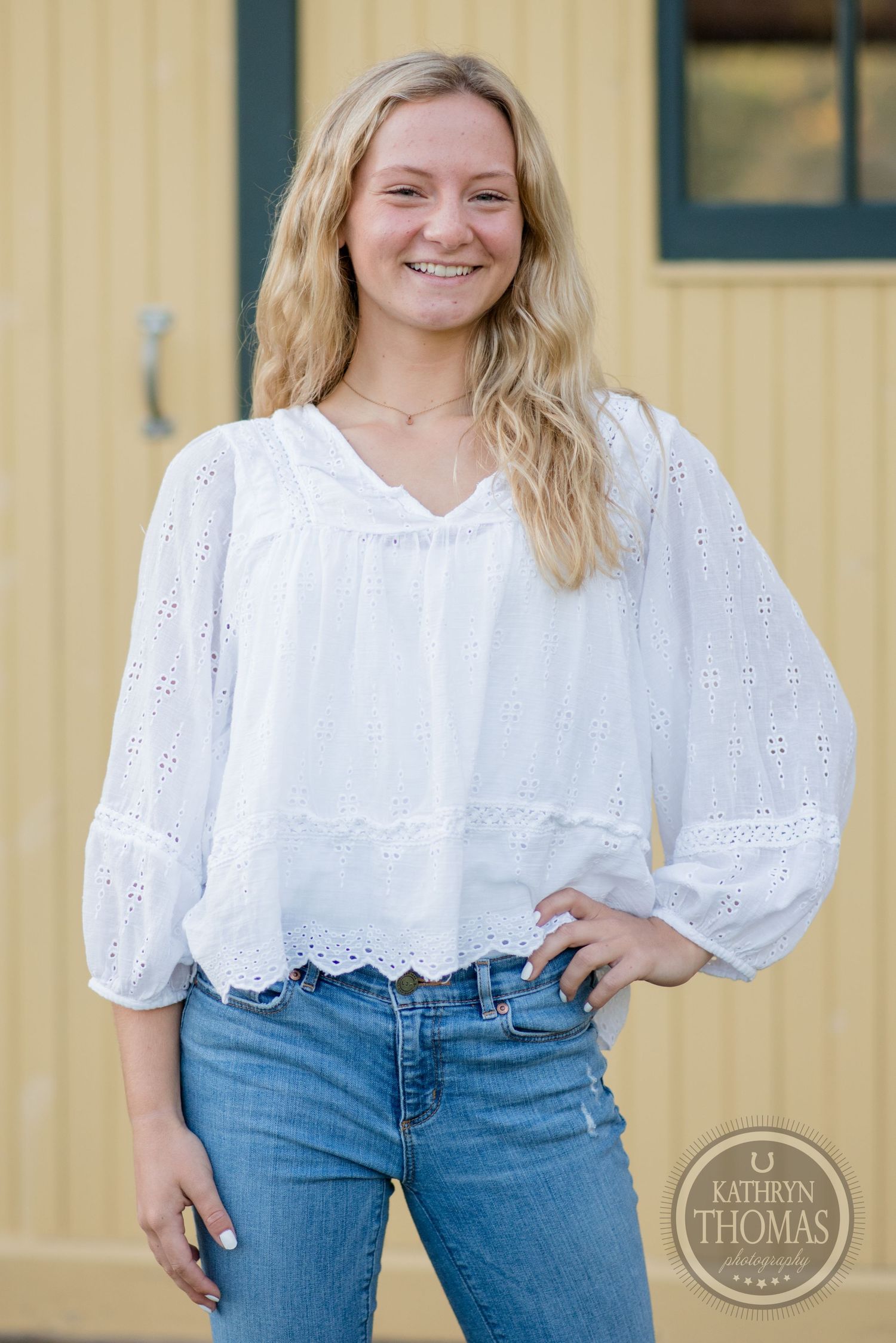 Summer fashion portrait featuring white eyelet blouse against yellow building exterior.