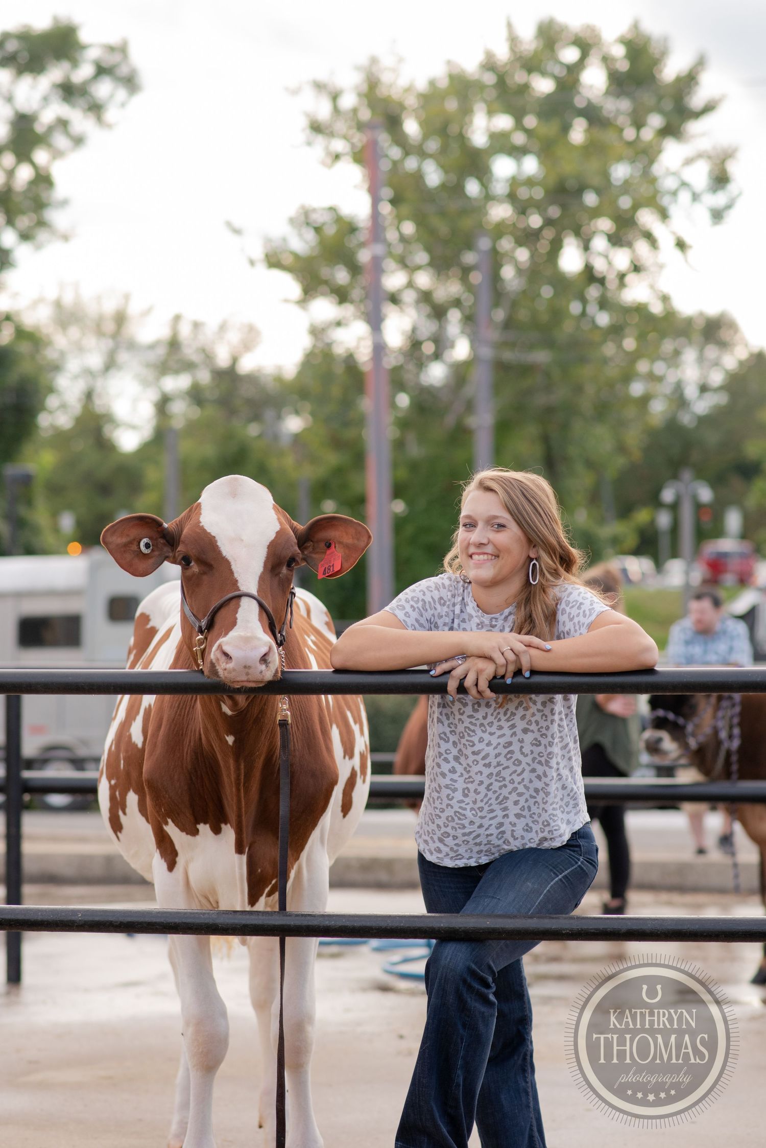 A Holstein dairy cow and person in casual attire lean against metal fencing at an outdoor event.