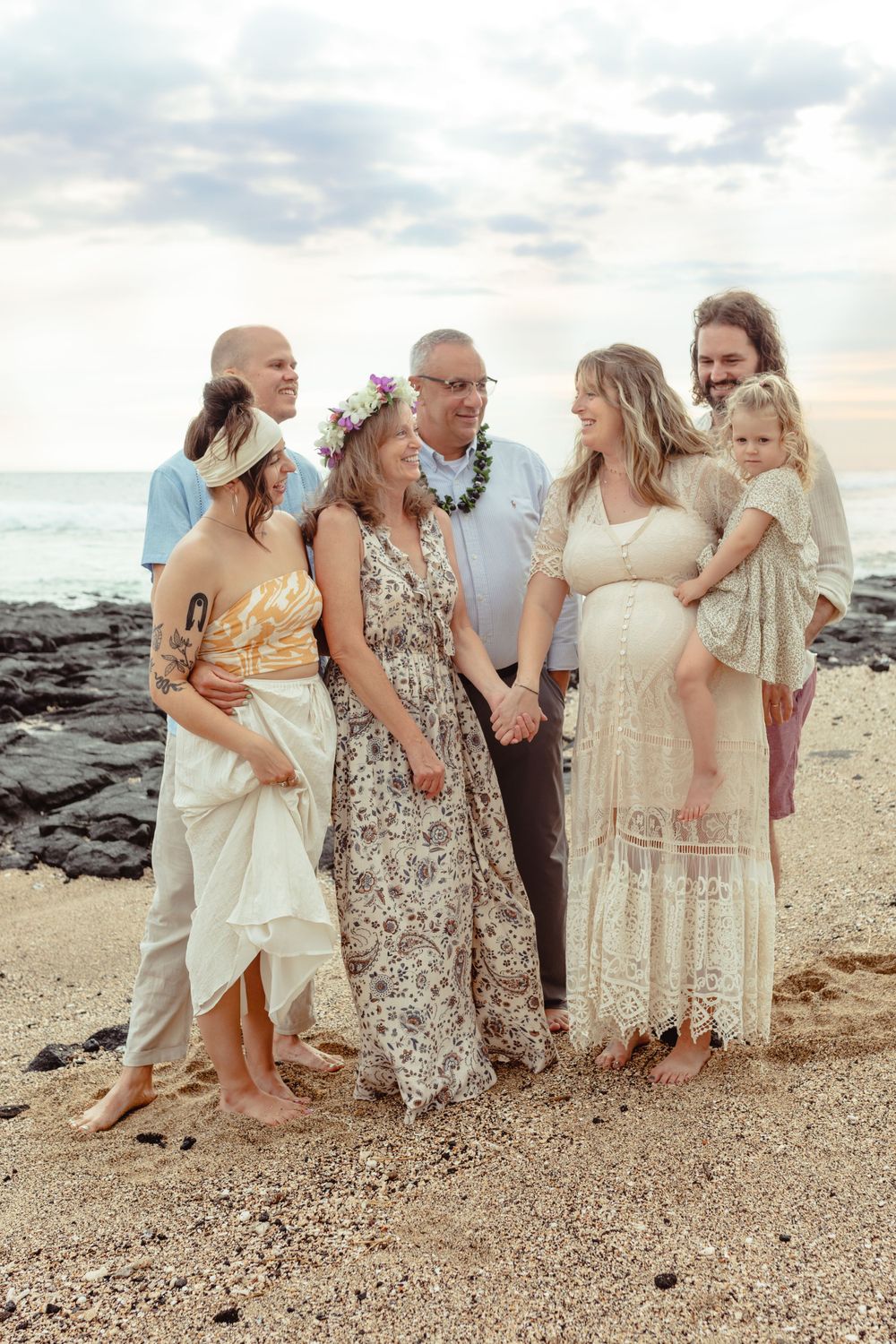 Extended family gathering on a Hawaiian beach at sunset wearing light flowy dresses.