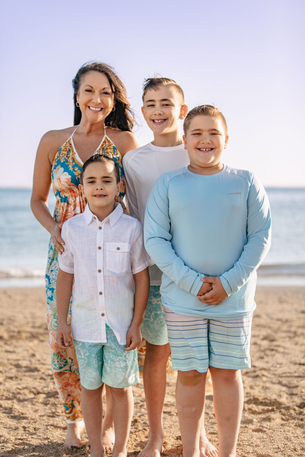 A group poses for a beach portrait wearing coordinated blue and white outfits.