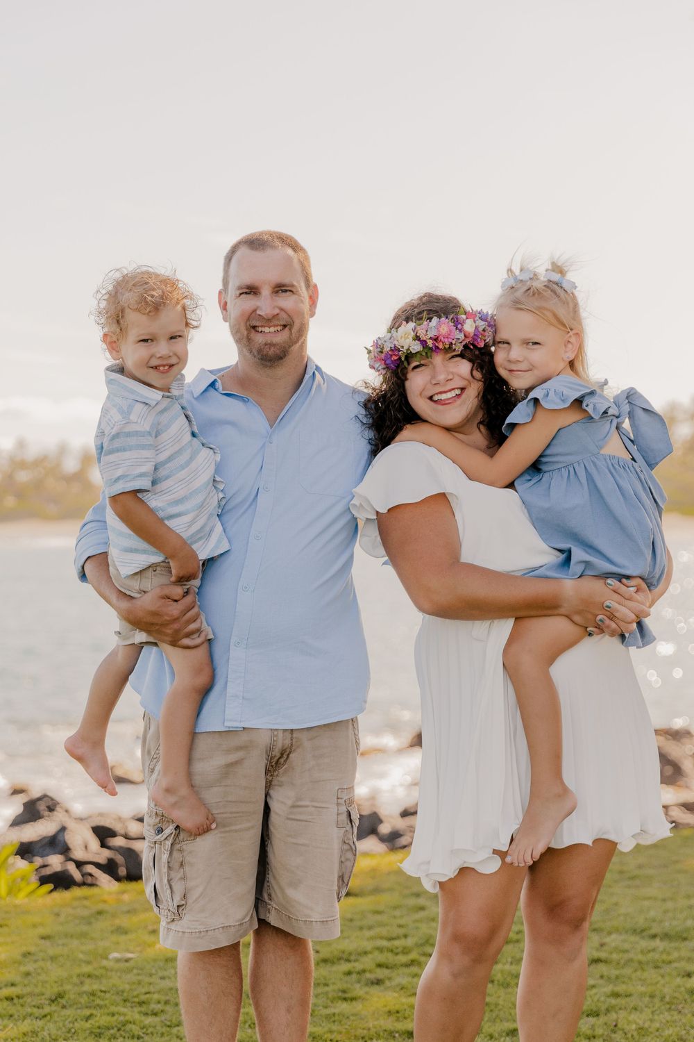 Family portrait on grassy lawn by the beach at sunset wearing coordinated blue and white outfits.