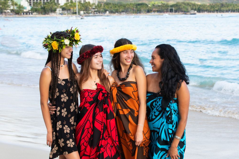 Group wearing flower crowns and tropical print dresses posing on Waikiki beach.