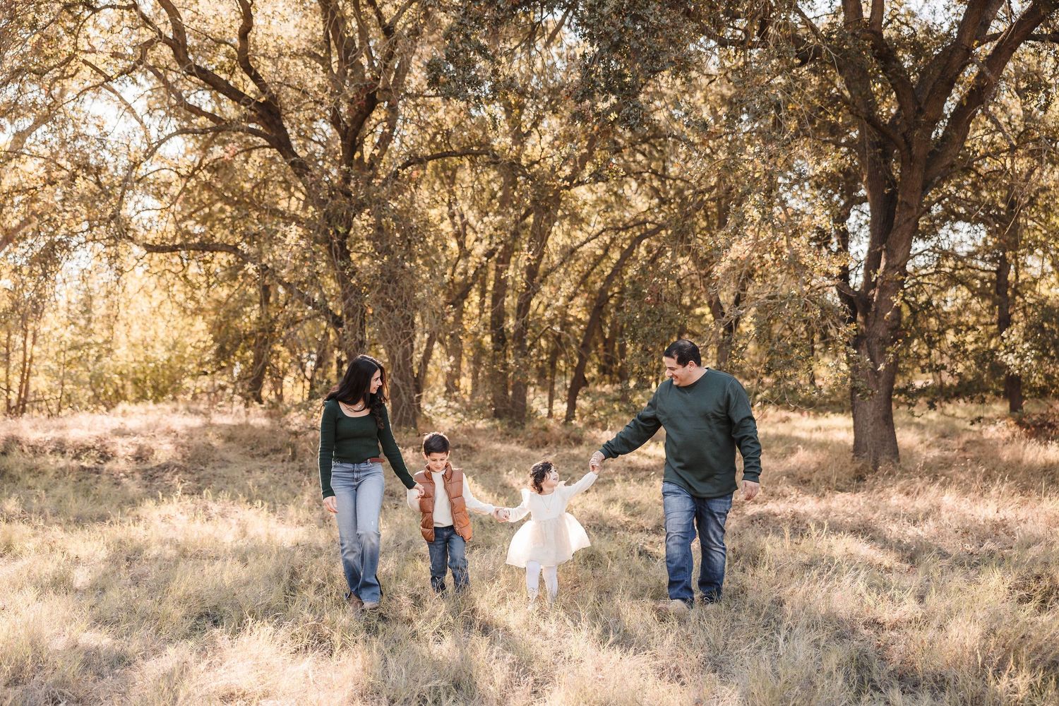 Family members walk hand in hand through a autumn field with oak trees in golden light.