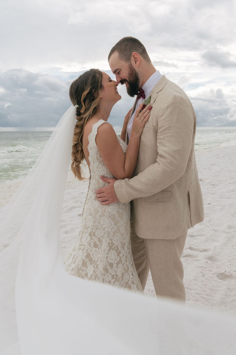 Romantic beach wedding scene with couple embracing on white sandy shore.