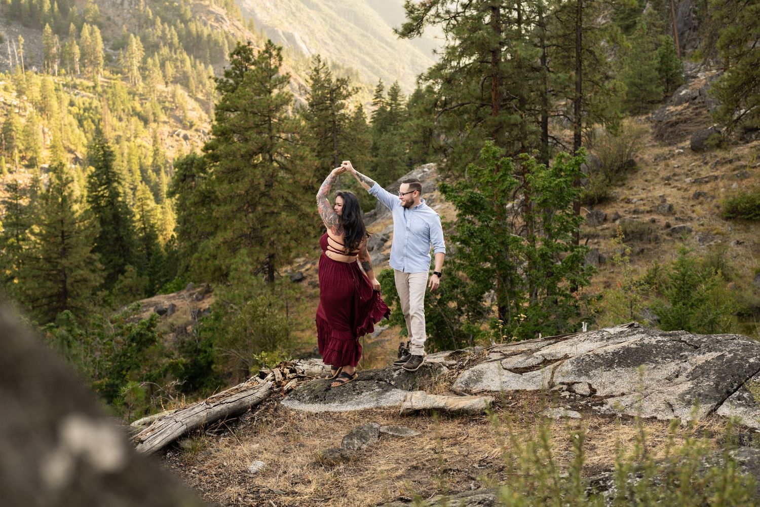 Joyful moment captured on rocky mountain outcrop with sunlit peaks and forest in background.