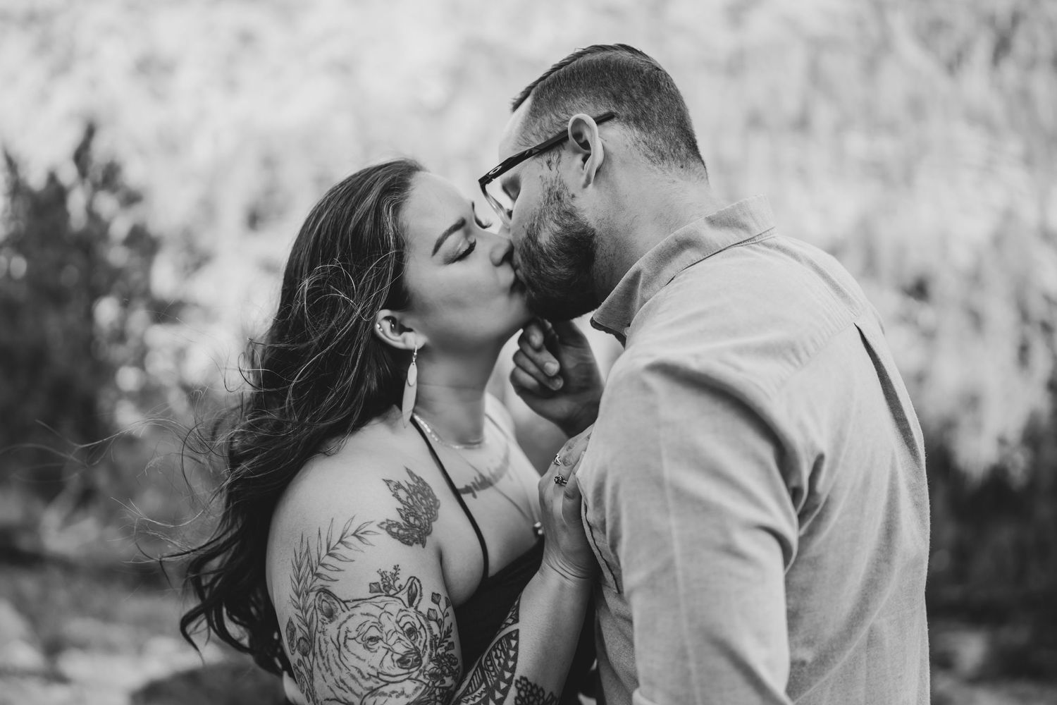 Close-up black and white photo of couple sharing intimate moment with mountain scenery behind.
