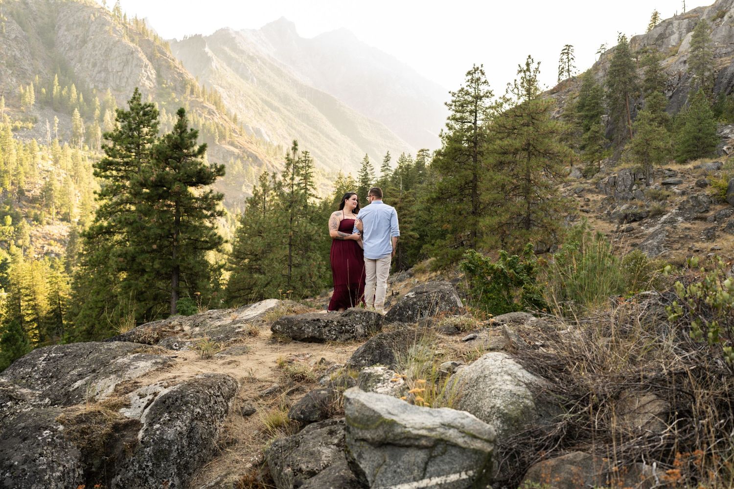 Couple enjoying scenic mountain vista while standing on rocky overlook at sunset.
