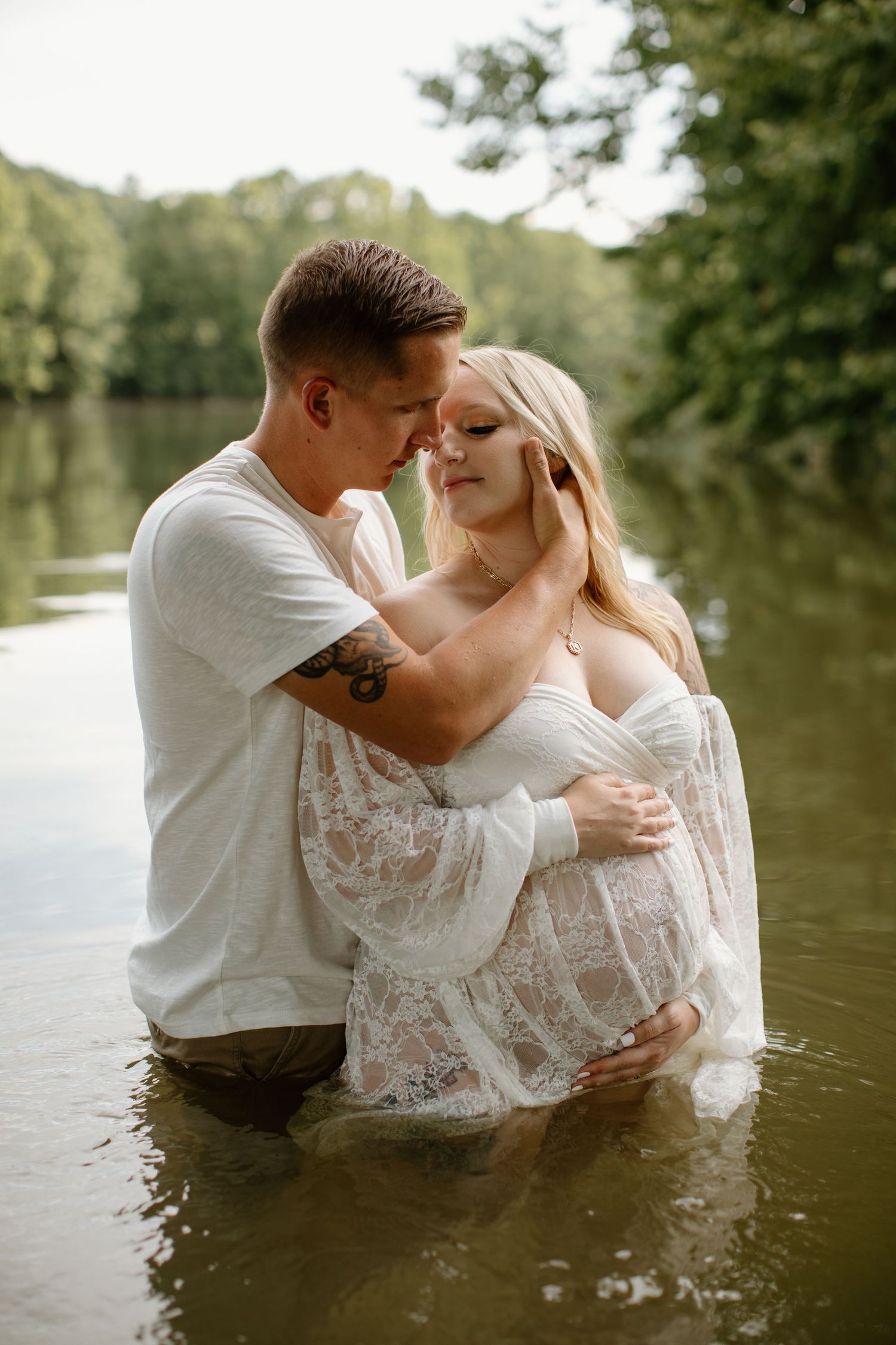 Romantic couple embracing during water photoshoot in white lace dress.