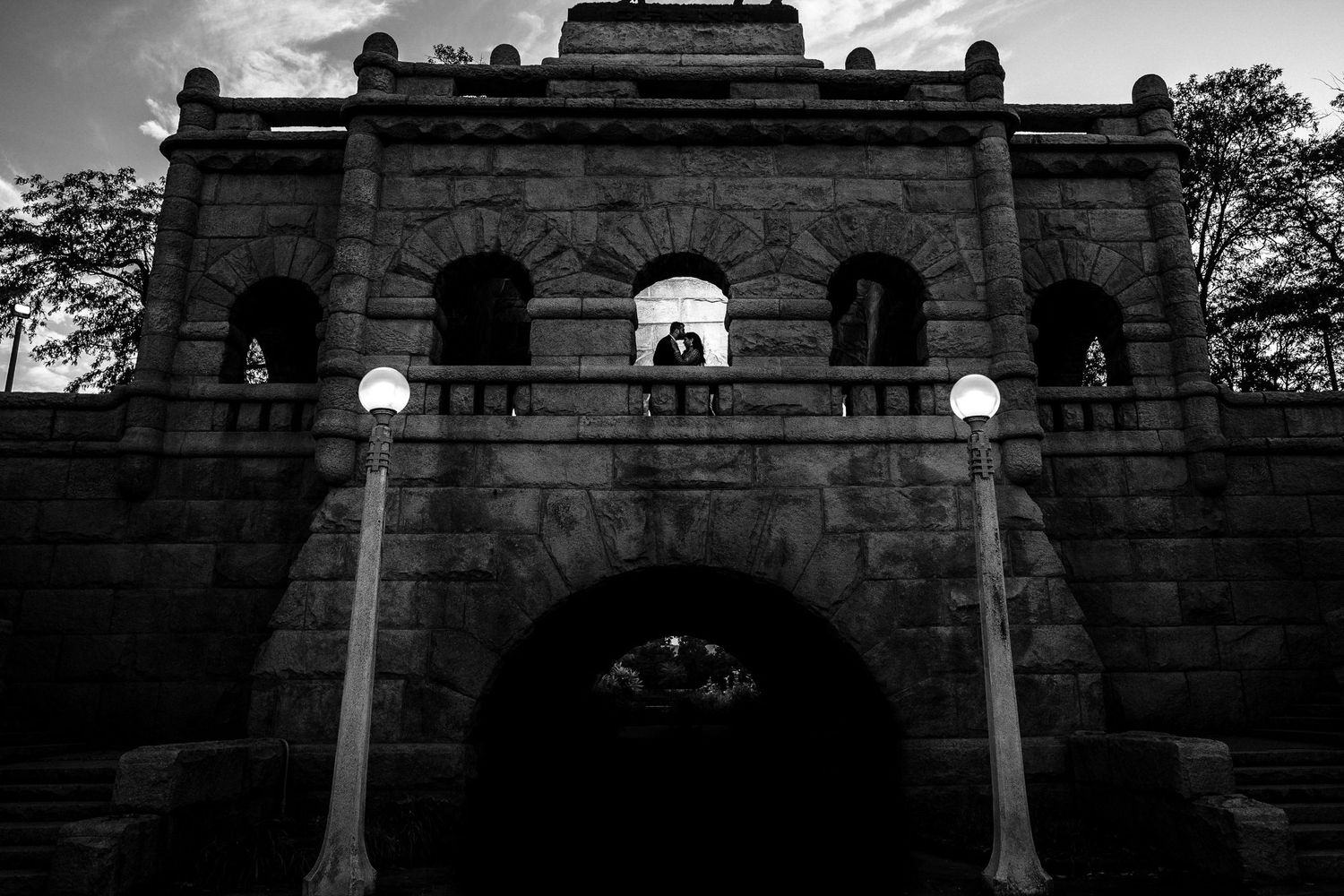 Backlit couple kisses under the archway atop a majestic castle, love's silhouette etched against a fairytale backdrop