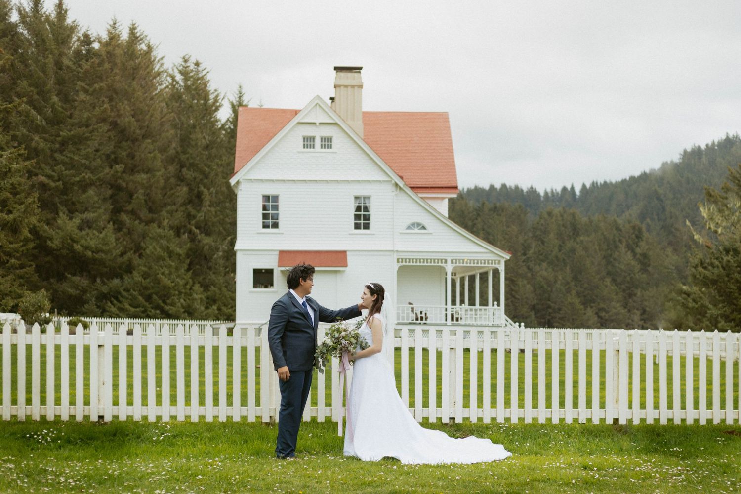 A charming white lighthouse keeper's house with picket fence against an overcast sky.
