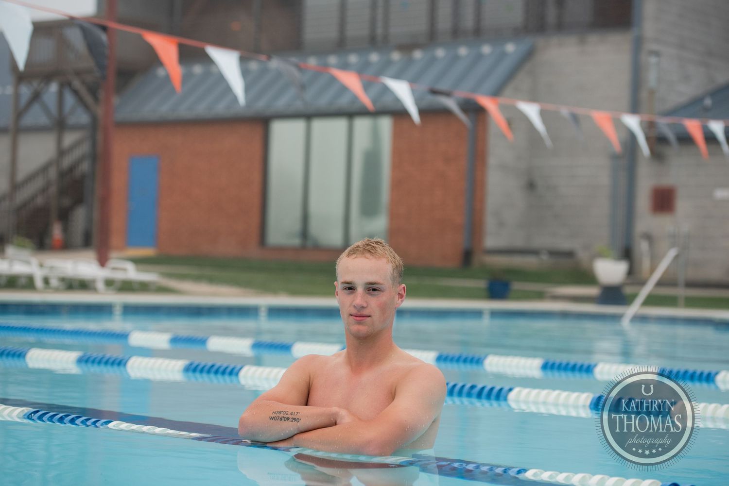 A swimmer poses in the pool with orange and white pennant flags visible overhead.