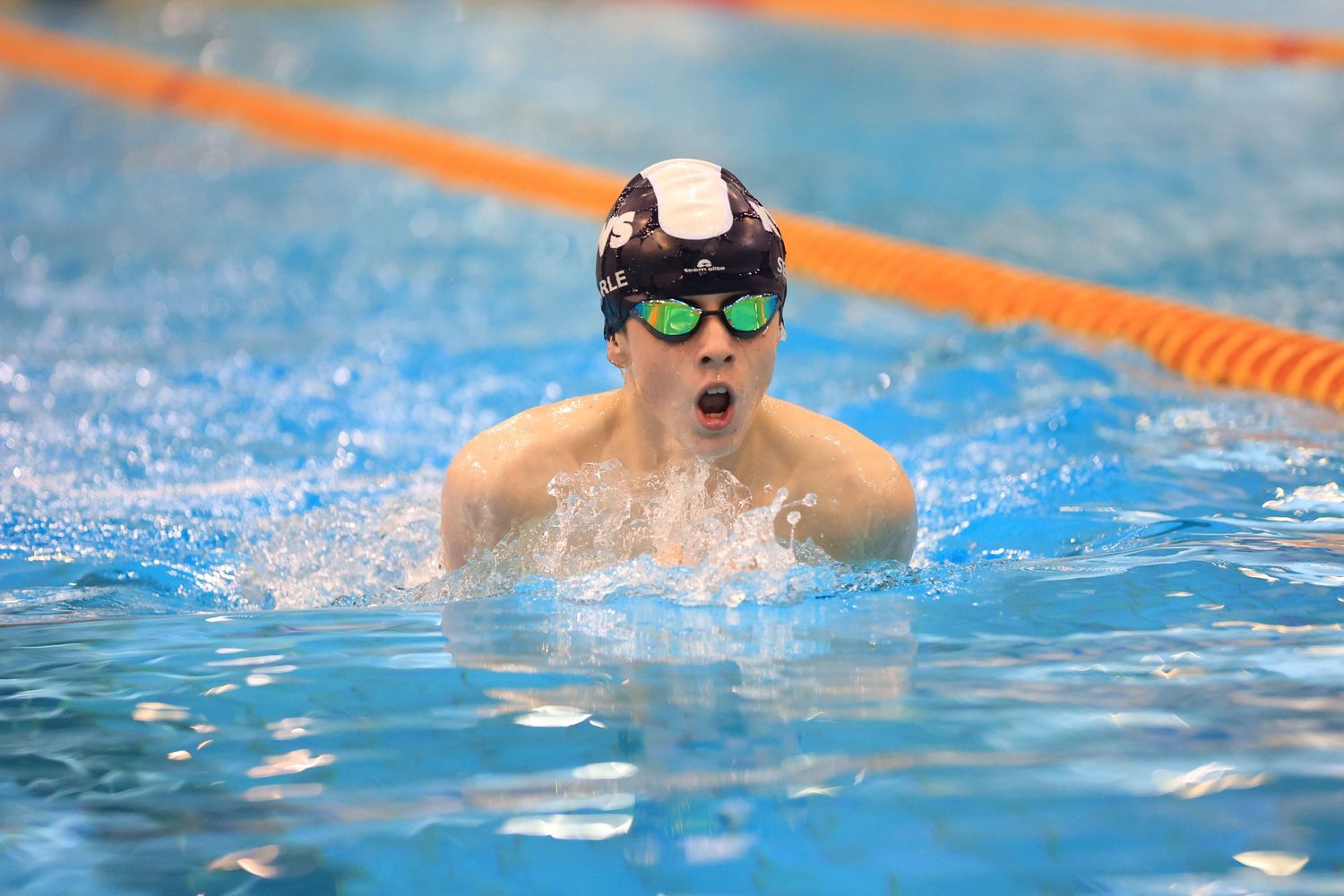 Swimmer performing breaststroke wearing goggles and cap during competition.