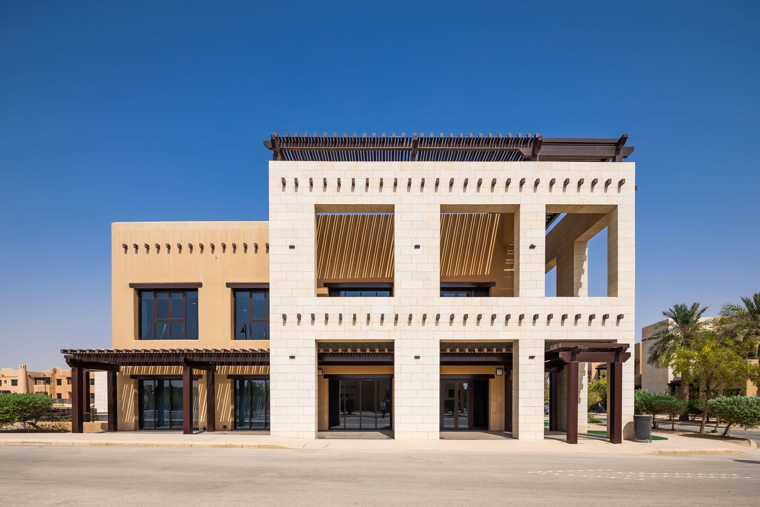Modern commercial building with traditional Arabic architectural elements and wooden shutters in beige tones.