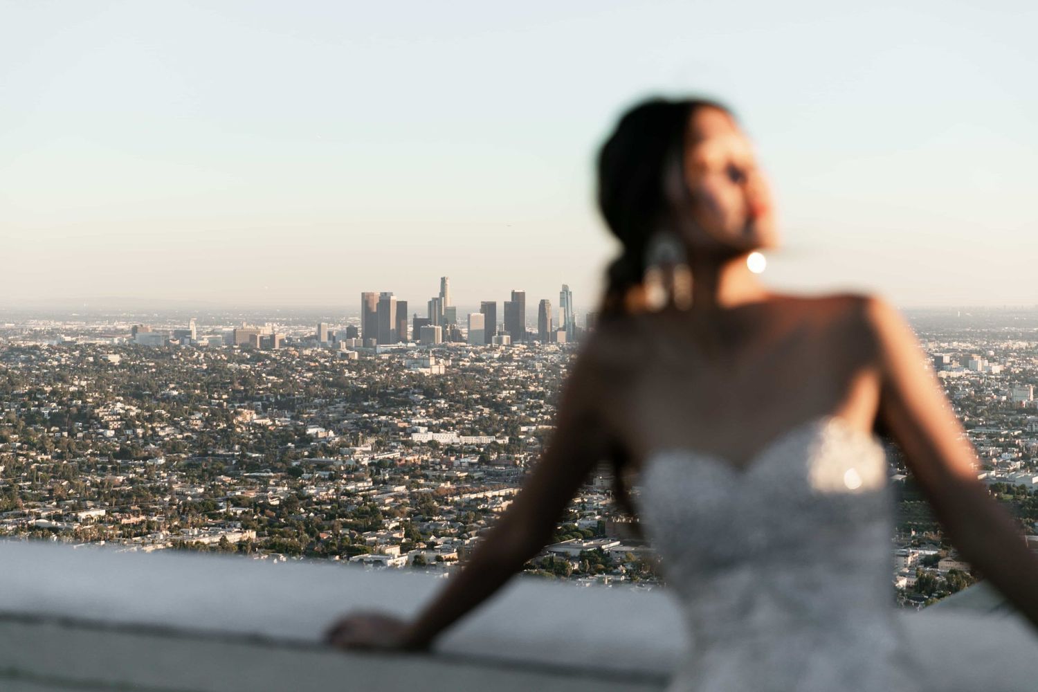 Bride in strapless lace wedding gown overlooks the Los Angeles city skyline at golden hour.