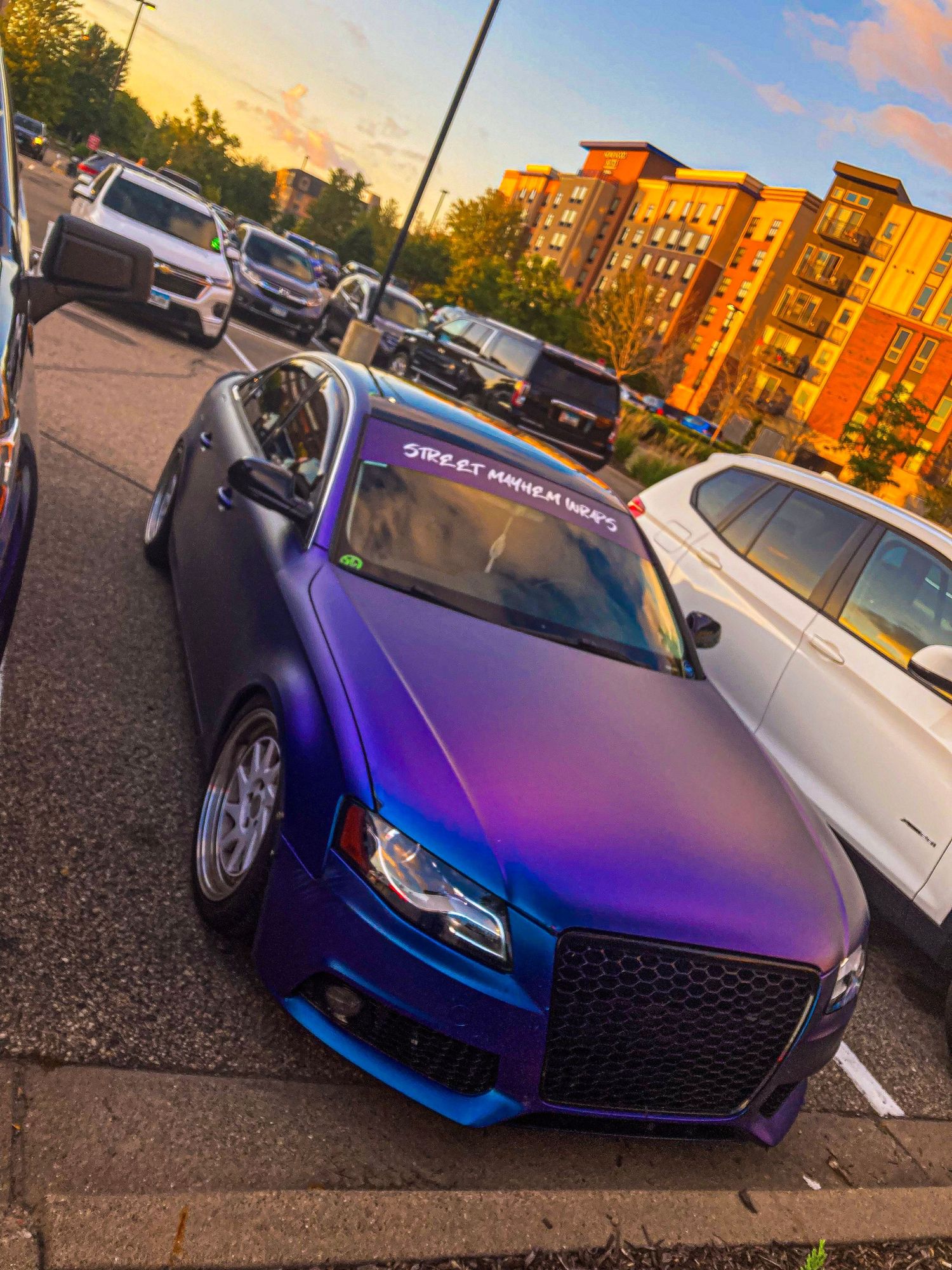 Matte purple Audi with custom grill parked in parking lot at golden hour.