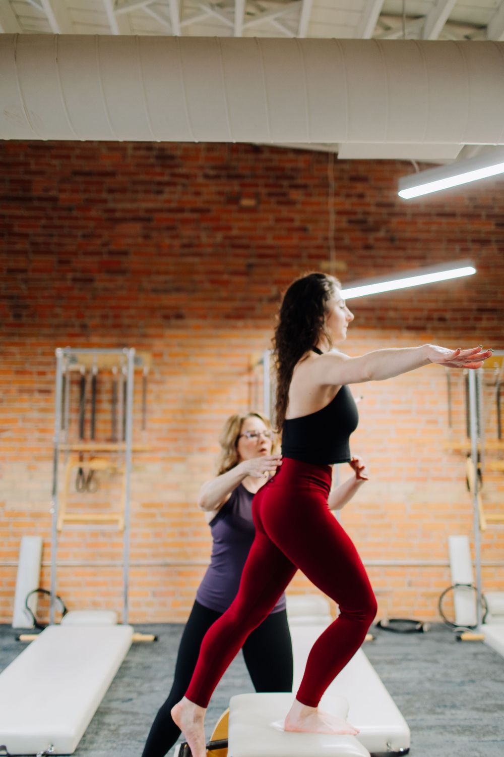 Instructor guiding student through Pilates movements on reformer equipment.