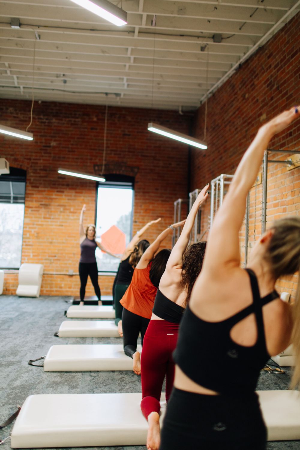 Group fitness class with participants stretching in unison on Pilates reformer machines.