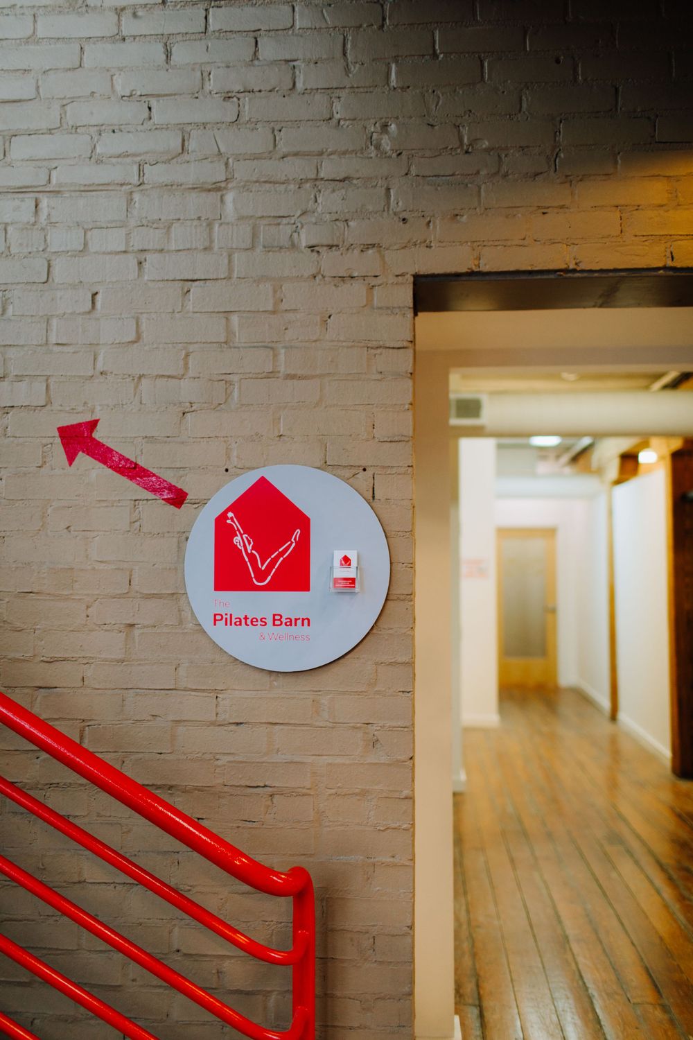 Red directional sign for Pilates Barn mounted on white brick wall.
