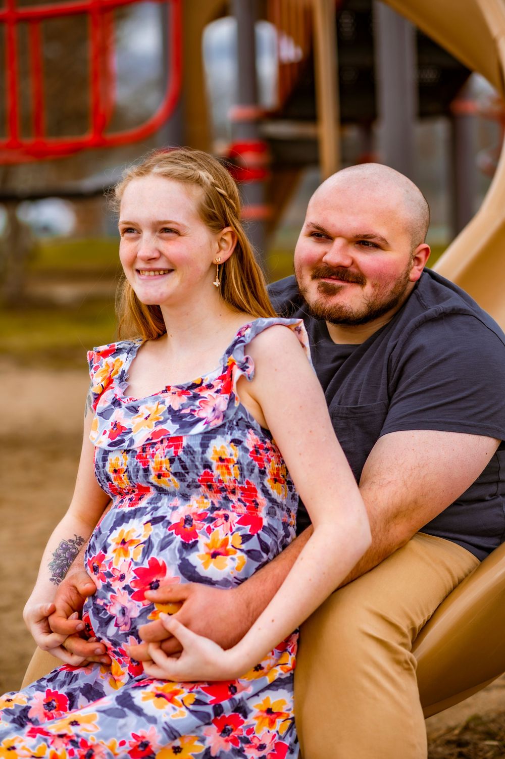 A couple poses together on playground equipment wearing casual attire.