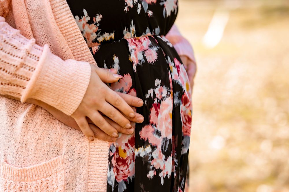 Close-up of hands resting on a floral dress maternity bump.