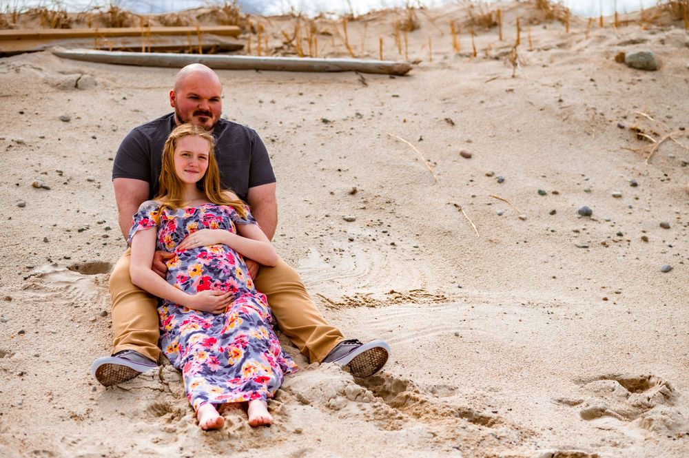 A couple sits together on sandy beach terrain wearing casual clothing.