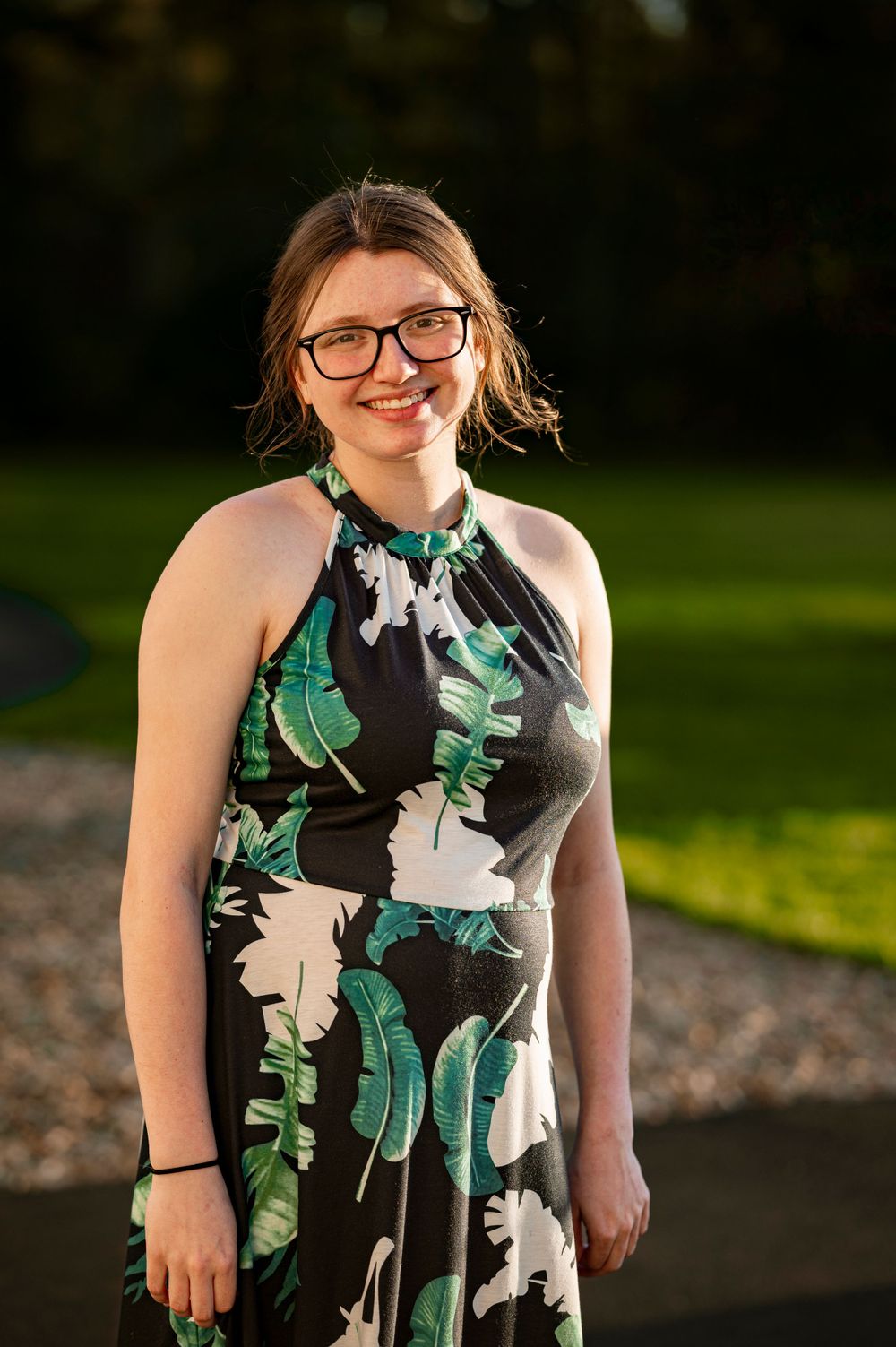 A person in a tropical print halter dress poses outdoors in warm sunlight.