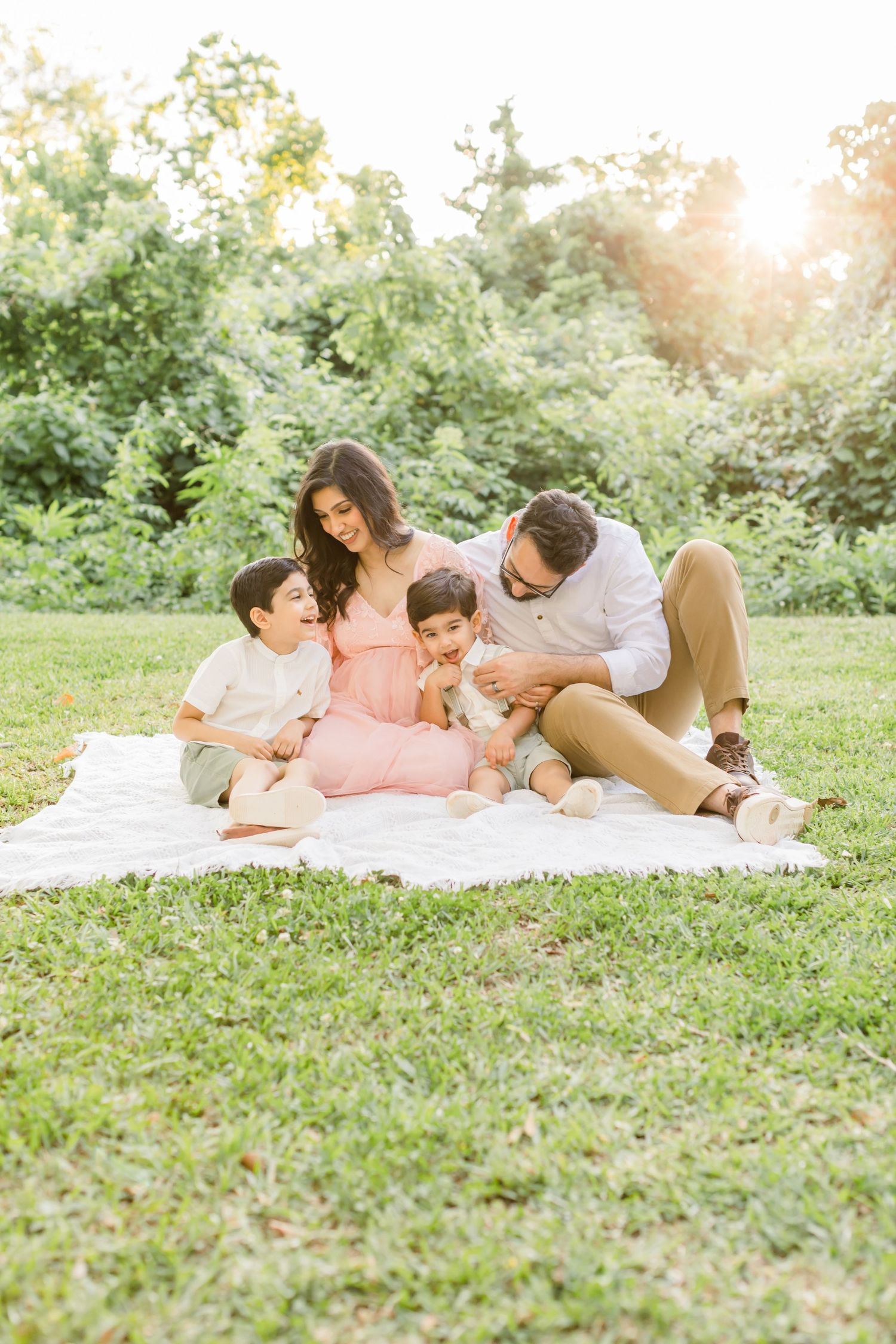 A family sits together on a white blanket for a sunset photo session in a lush garden setting.