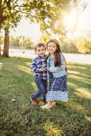 Two children playing and laughing together on a grassy hill during golden hour sunset.