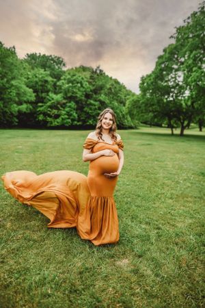 A flowing orange dress creates movement against a green lawn during a photo session.