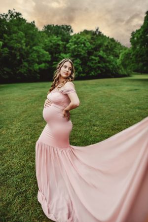 A flowing pink dress twirls gracefully against a backdrop of green trees and cloudy skies.