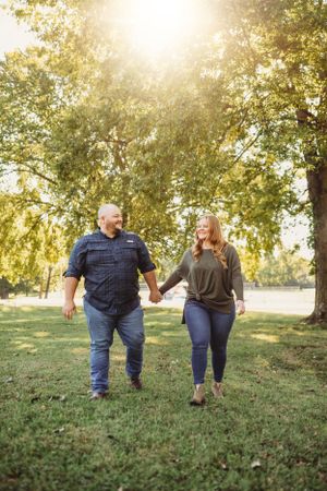 Couple walking hand in hand on a grassy hillside during sunset.