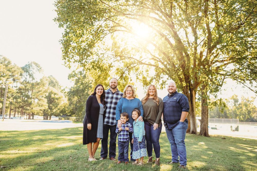 A multi-generational family poses together for a portrait in a sunny park setting.