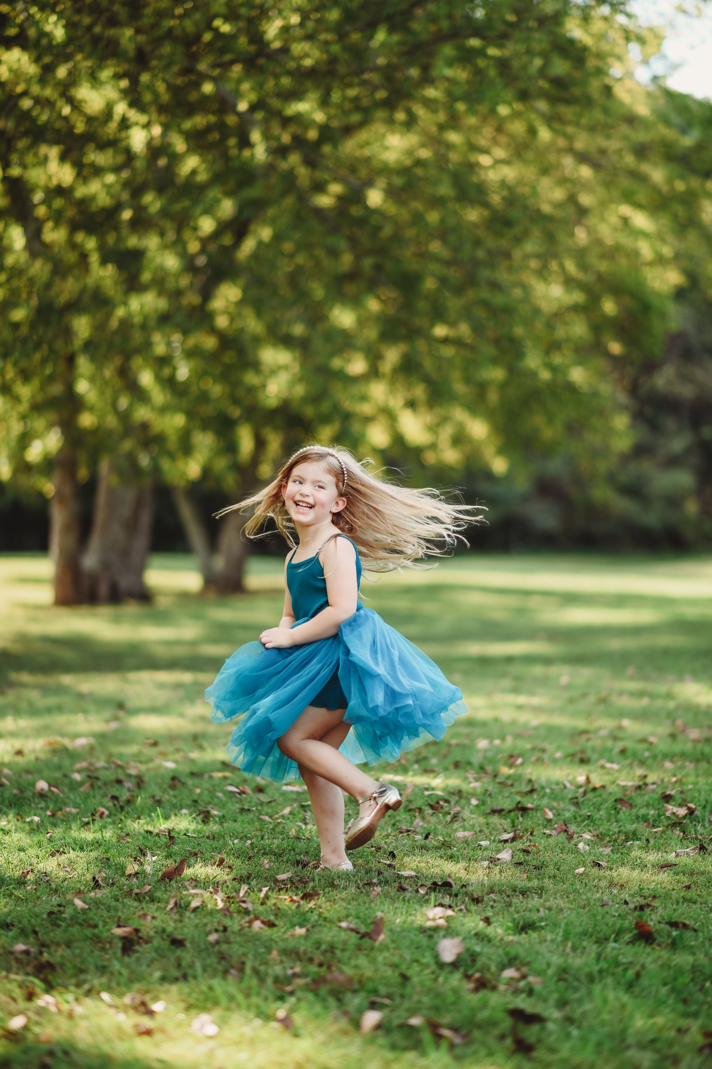 Young dancer in flowing blue dress twirling on grassy hillside.