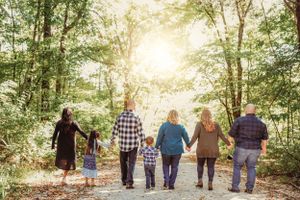 Family walking together through a wooded area with sunlight filtering through the trees.