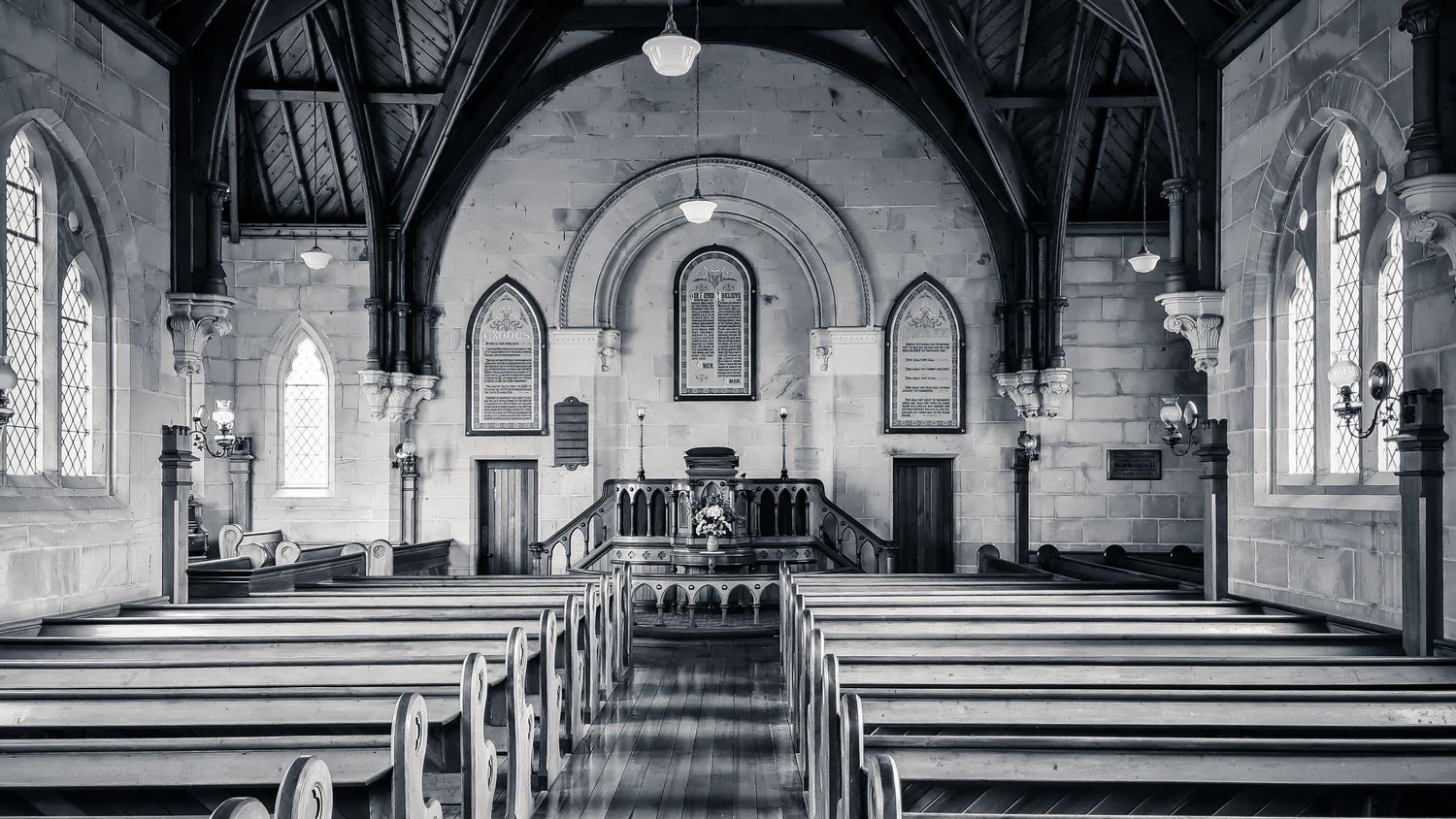 Empty church interior with wooden pews and arched ceiling in black and white.