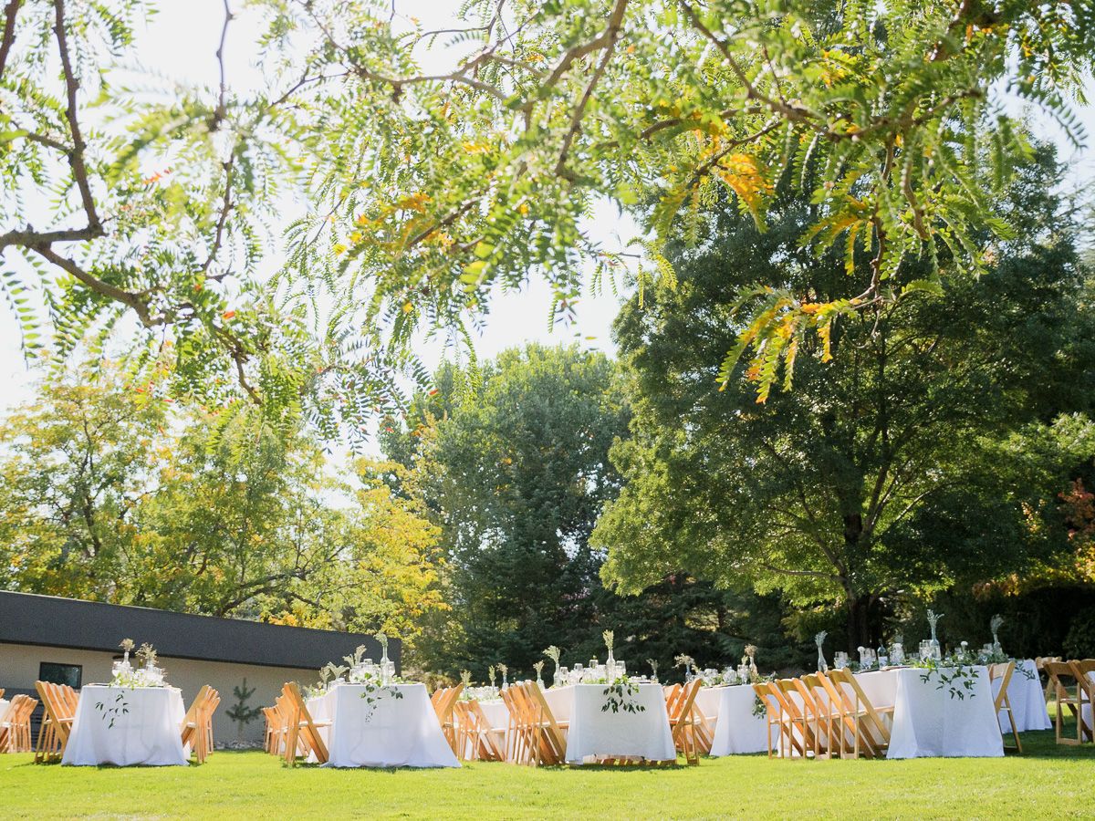 White round dining tables set up on a lawn under trees for an elegant outdoor garden wedding reception.