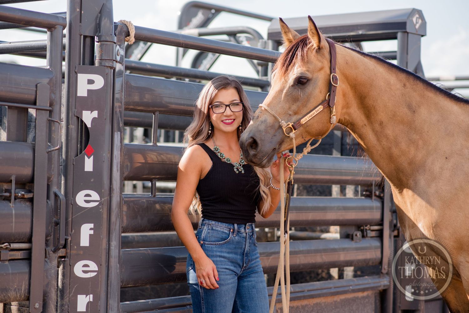 A palomino horse and someone in casual attire pose together near metal horse stalls.
